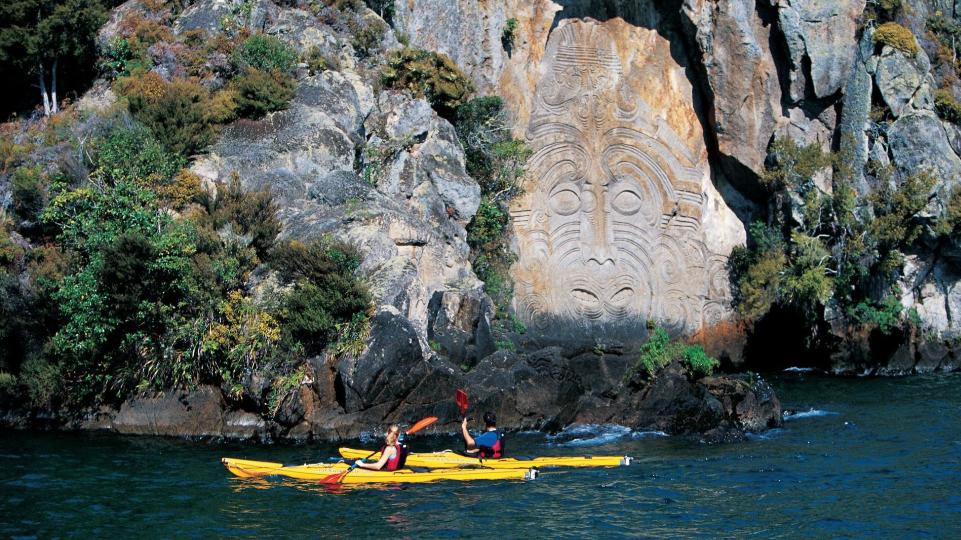 Kayakers admiring Māori rock carvings at Mine Bay, Lake Taupō