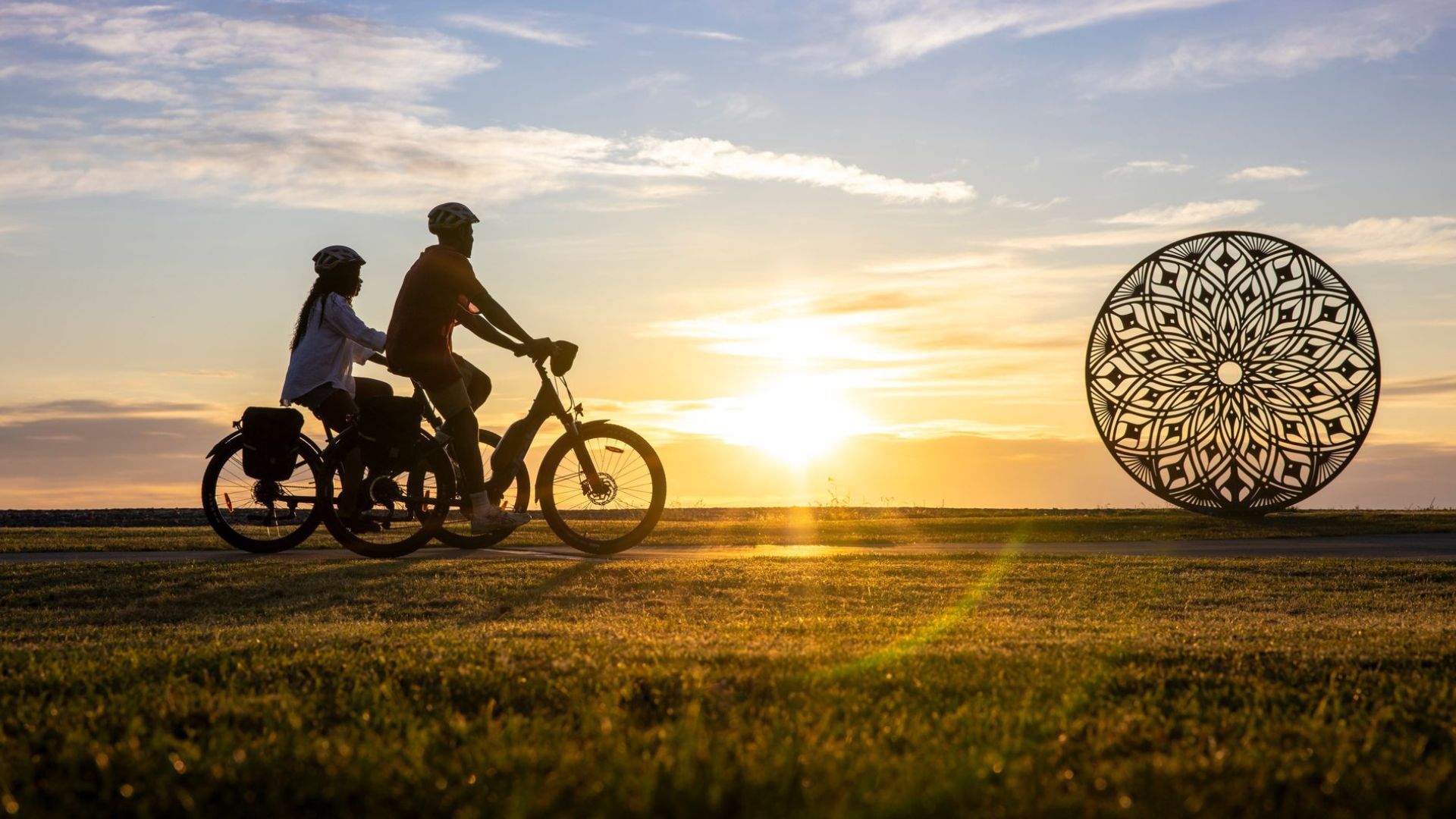 Cyclists riding along Napier’s waterfront at sunset with Art Deco sculpture